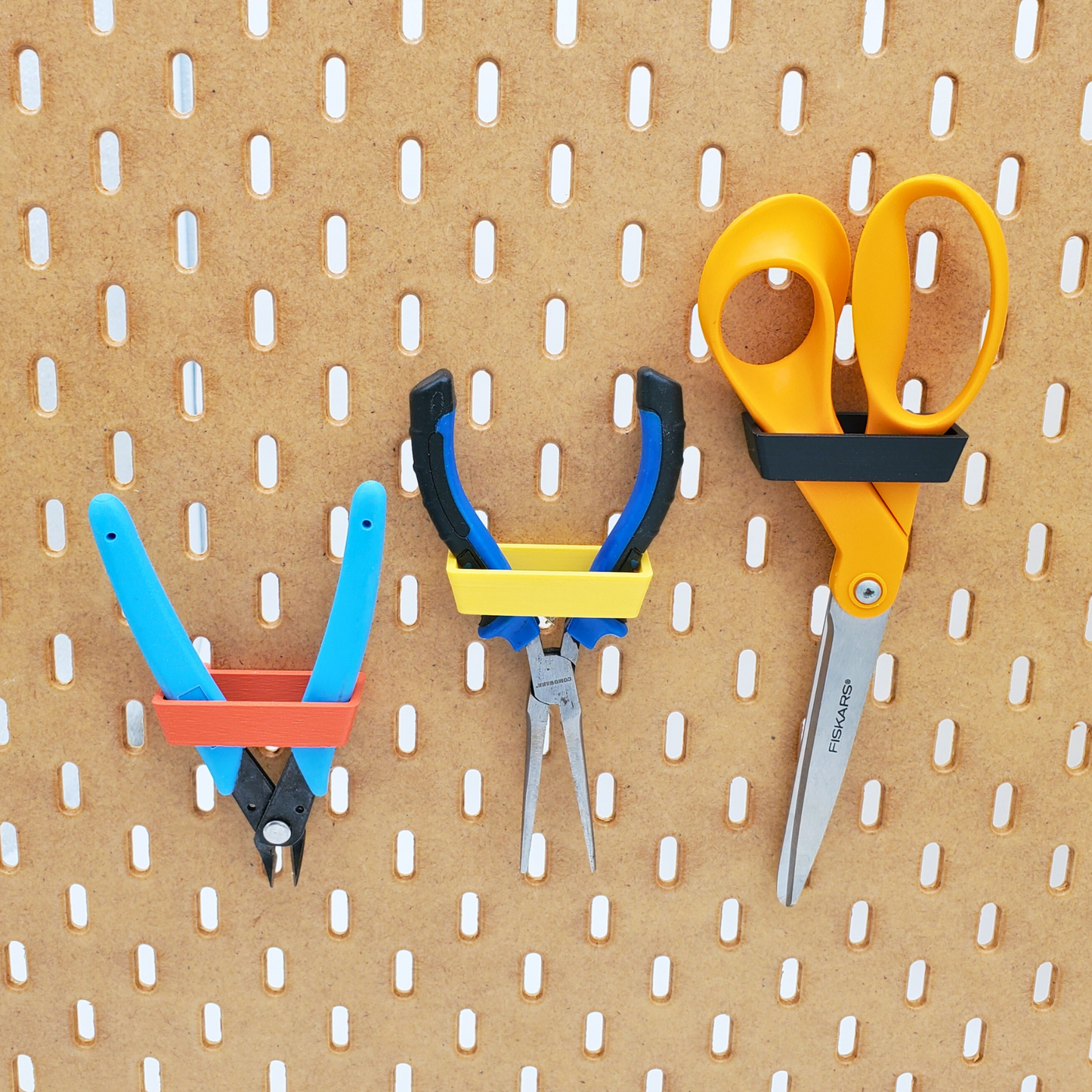Muted Red holding blue snips on bottom left. Savannah Yellow holding blue.black pliers in middle. Charcoal black Skadis accessory holding orange scissor on top right.