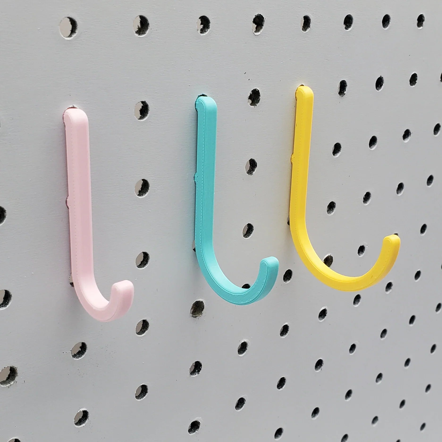 Small, Medium, and Large J Hooks in Light Pink, Teal, and Savannah Yellow on 1/4" pegboard.