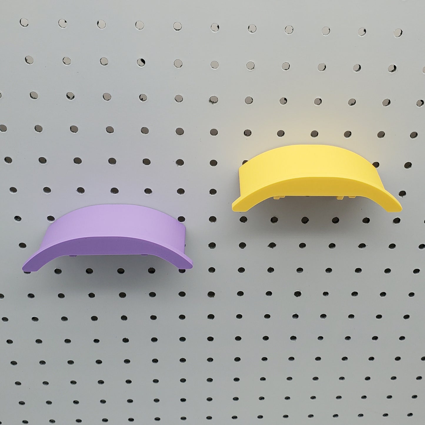 A yellow and a purple headphone holders on a 1/4" pegboard