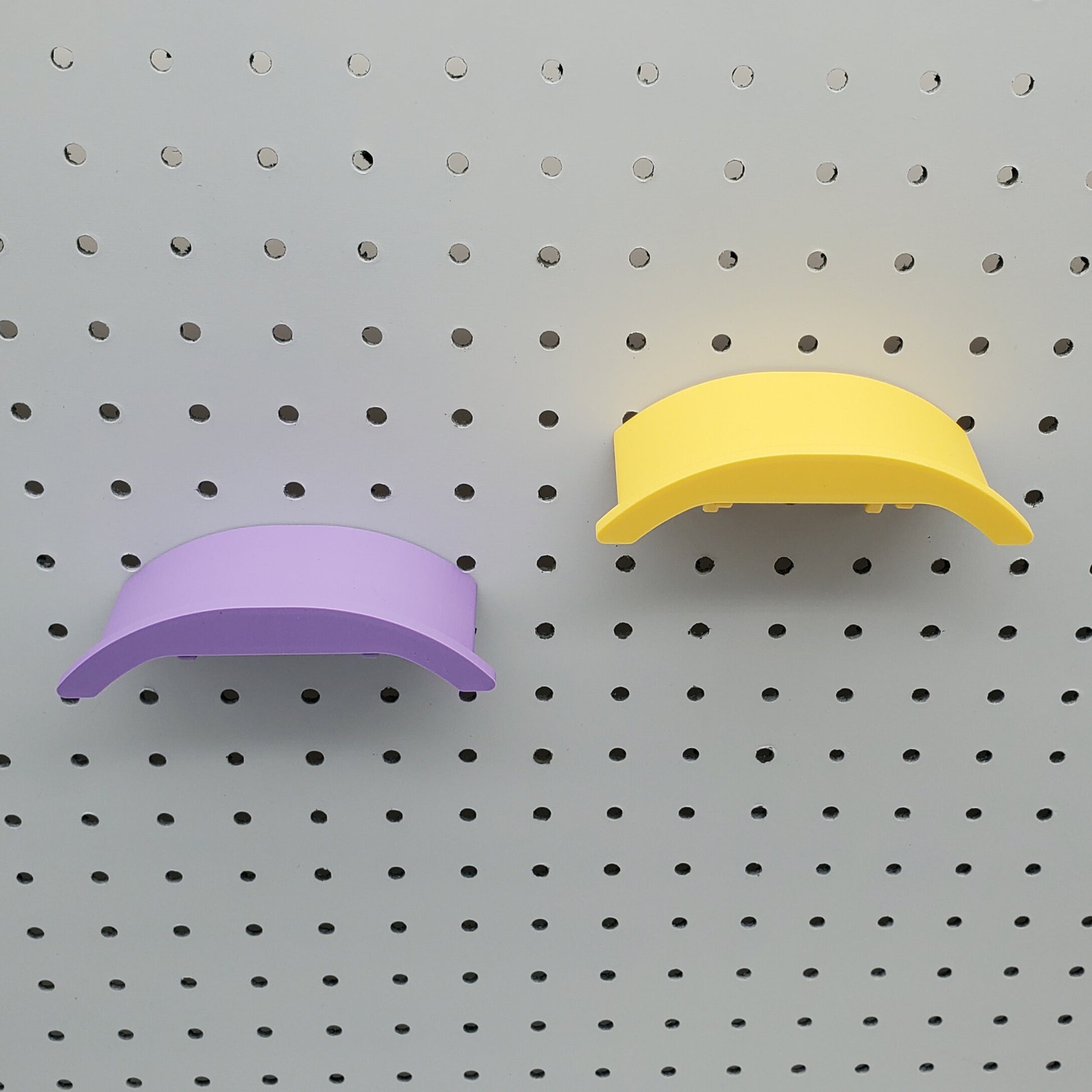 A yellow and a purple headphone holders on a 1/4" pegboard