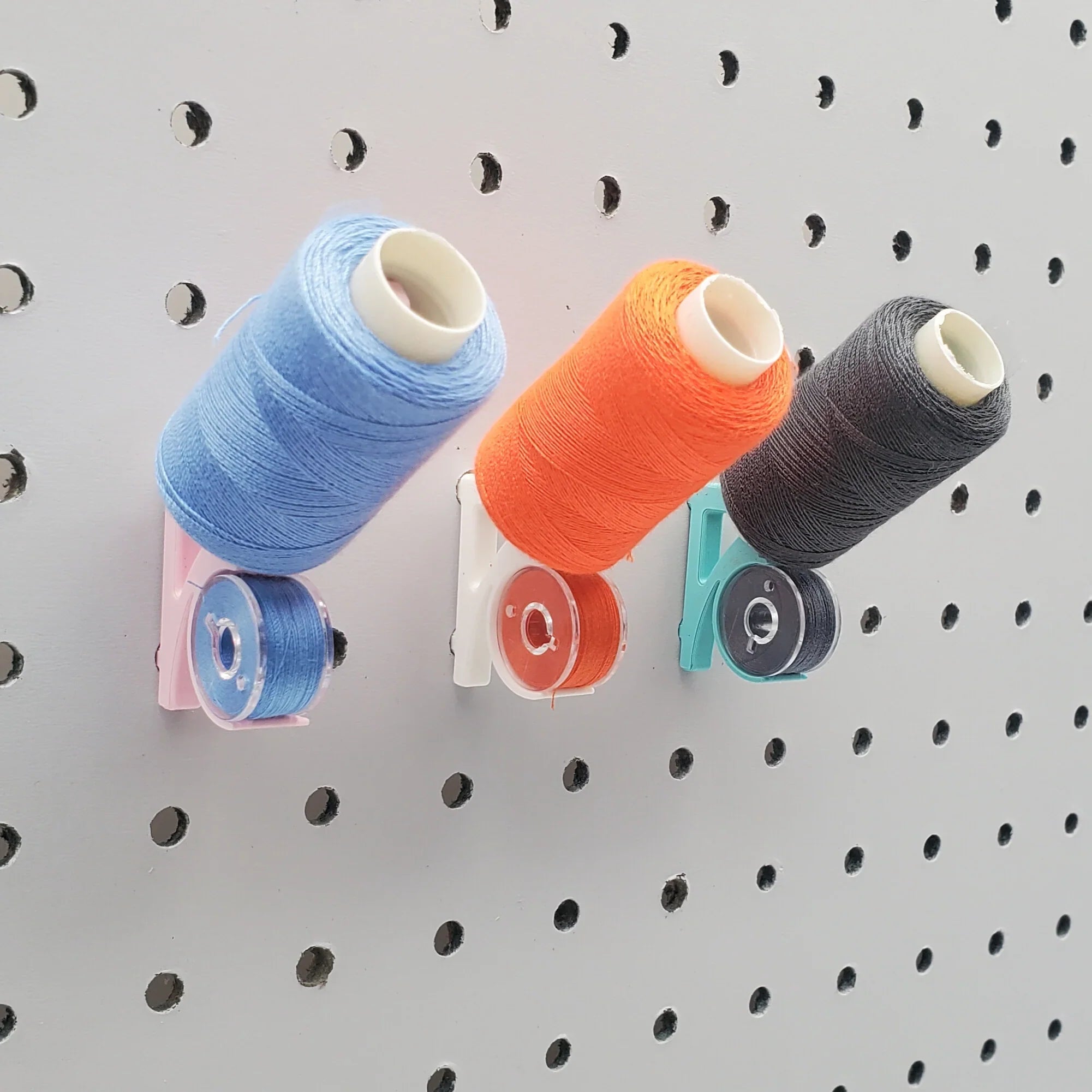 Tilted Thread and Bobbin Storage Hook in Light Pink, Cotton White, and Teal on 1/4" pegboard with thread spools and bobbins.