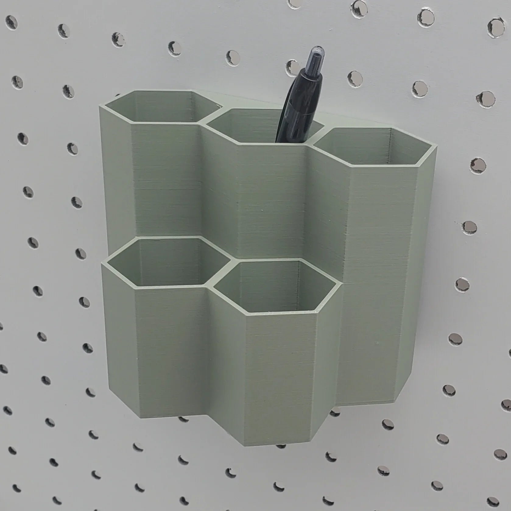 Tall Hexagon Tiered Pen and Pencil Organizer in Muted Green on 1/4" Pegboard with pen.
