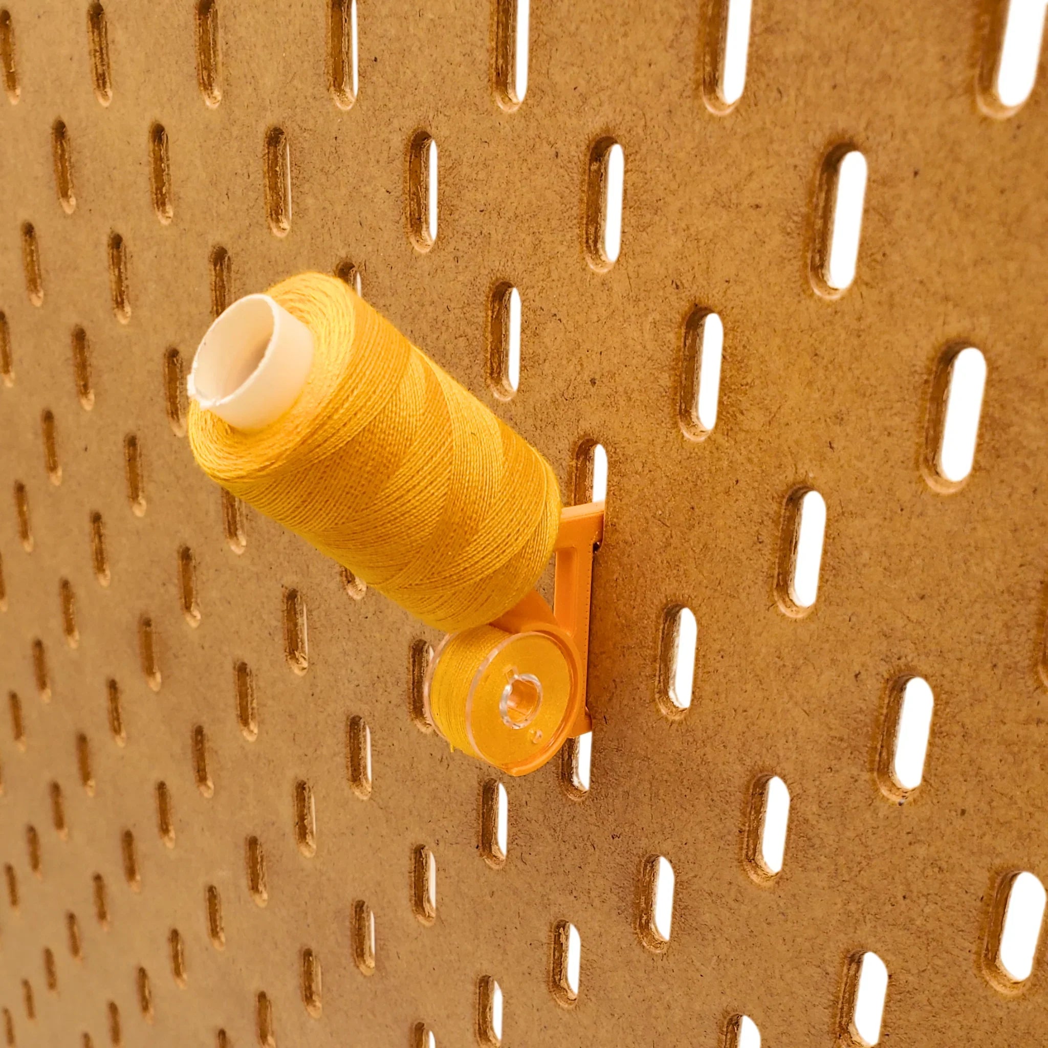 Tilted Thread and Bobbin Storage Hook in Sunrise Orange on IKEA SKADIS pegboard with orange spool and bobbin.