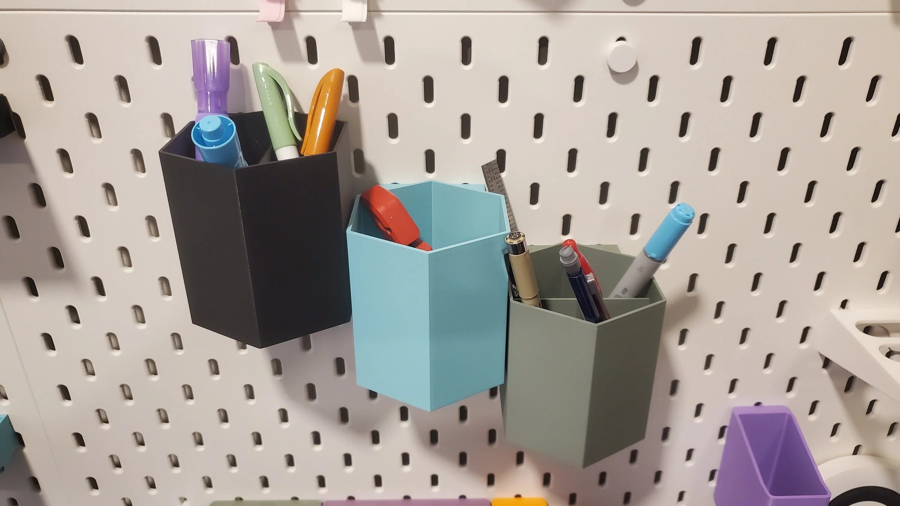 Three Hexagon Pencil Cups on IKEA SKADIS pegboard. Half Pot in Charcoal Black, Quarter Pot in Muted Green. and Half Pot in Light Blue on IKEA SKADIS pegboard with pens and pencils.